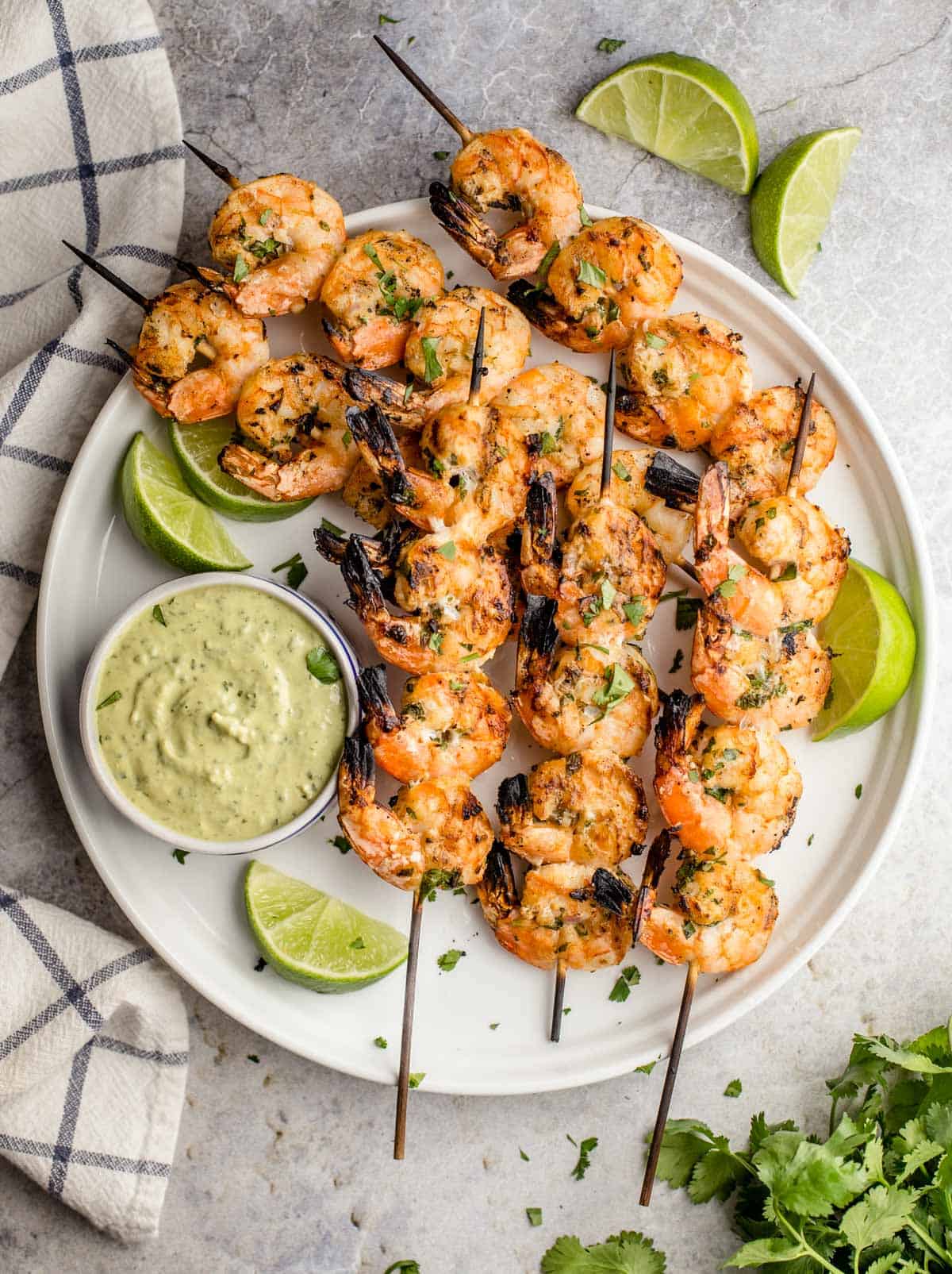 Cilantro Lime Shrimp on skewers on a white plate with a side of avocado cilantro dipping sauce
