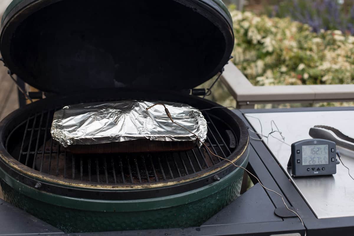 A pan filled with braised chuck roast, covered in aluminum foil, on the smoker