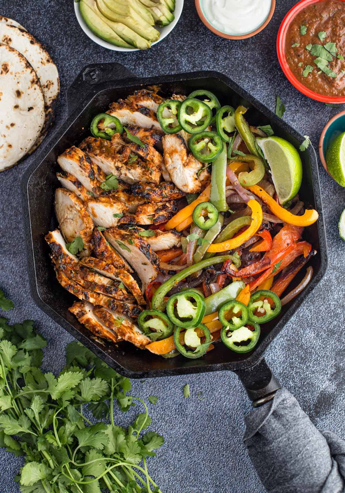 Grilled Chicken Fajitas with vegetables in a cast iron pan surrounded by fajita toppings