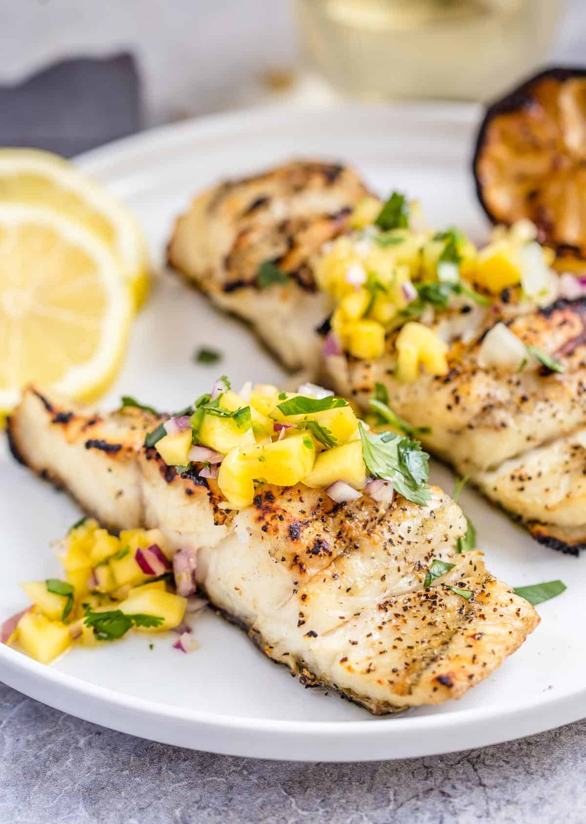 Two Grilled Halibut filets on a white plate and topped with a Mango Citrus Salsa