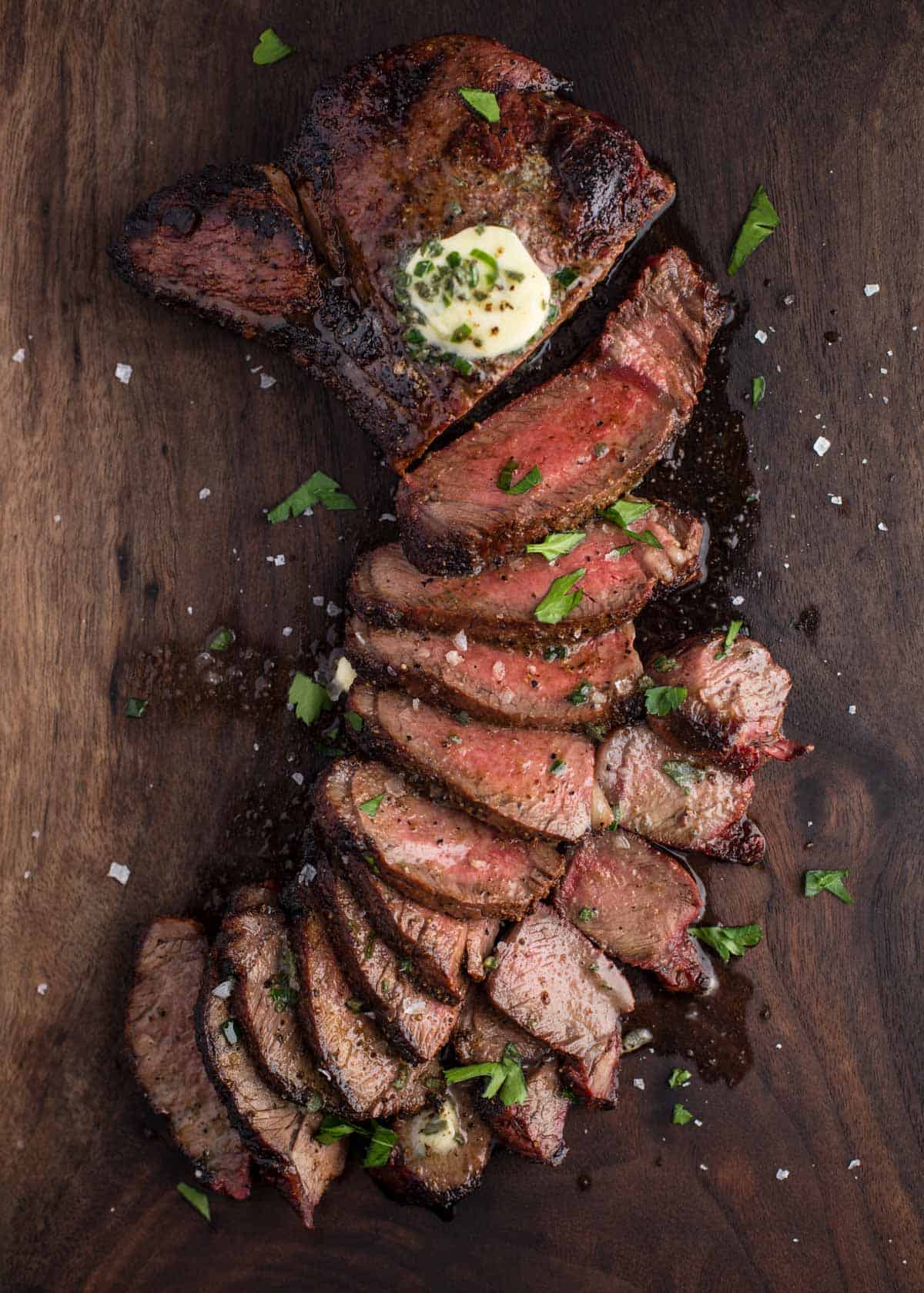 Slices of a Grilled Sirloin Steak on a cutting board and topped with an herbed compound butter