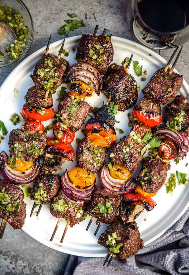 Steak Kebabs (Skewers) on a white round plate topped with a jalapeño chimichurri sauce