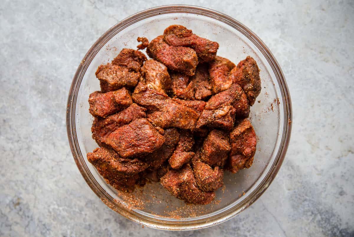 Cubes of seasoned raw beef cubes in a glass bowl