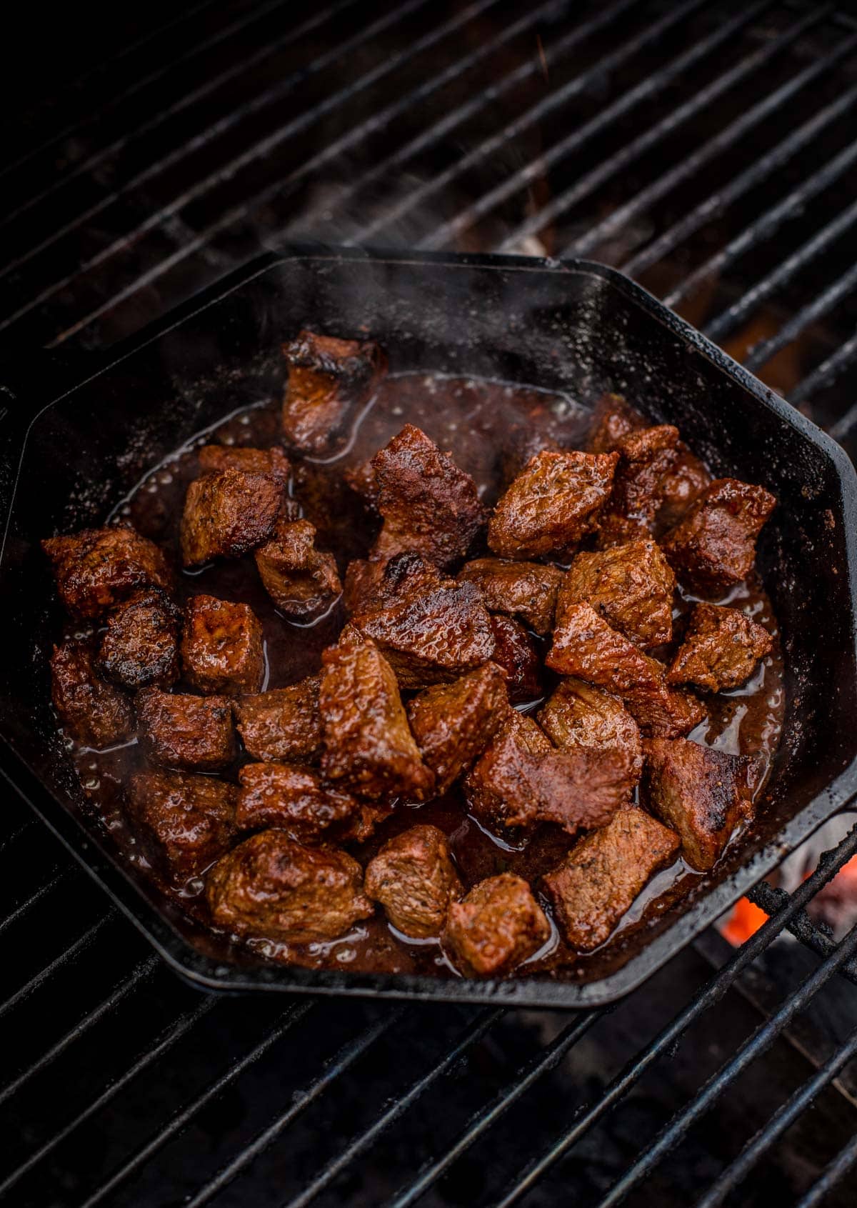 Steak bites in a cast iron pan cooking on the grill