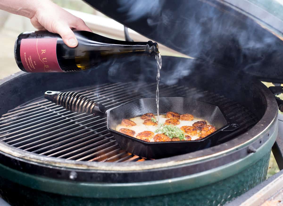 pouring wine in a hot cast iron pan with grilled scallops