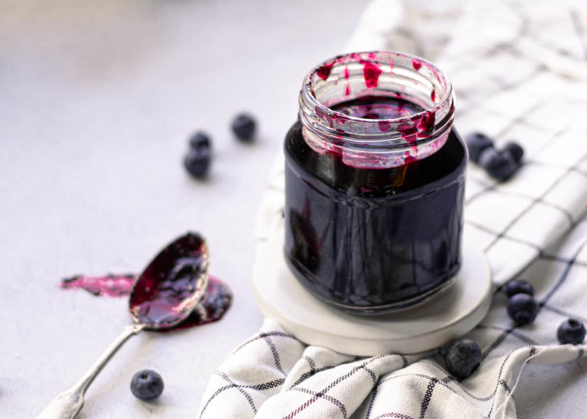 Blueberry simple syrup on a spoon on a cutting board.