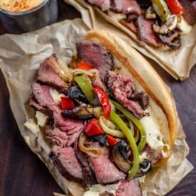 Two cheese steak sandwiched on a serving platter with toppings.