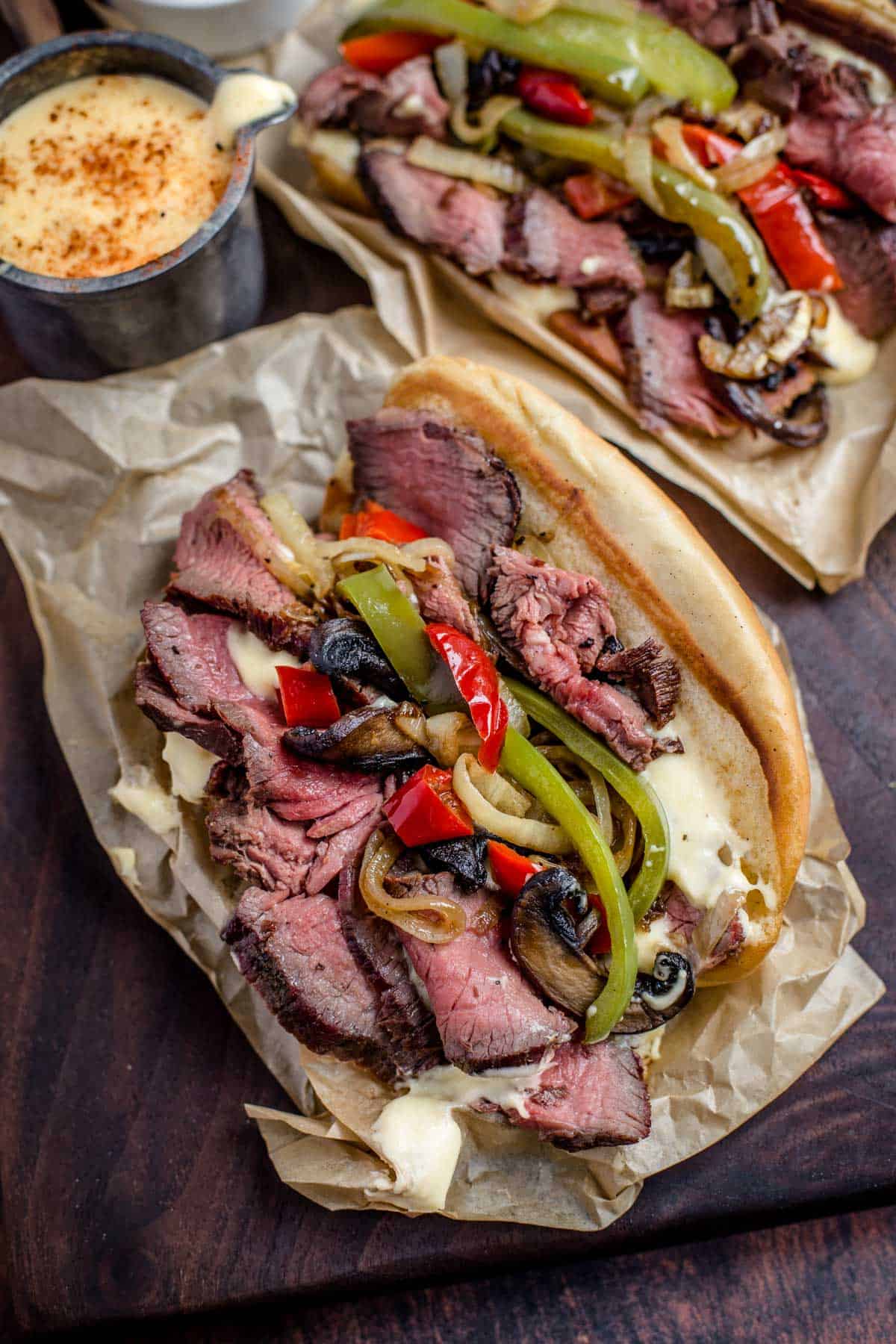 Two cheese steak sandwiched on a serving platter with toppings.