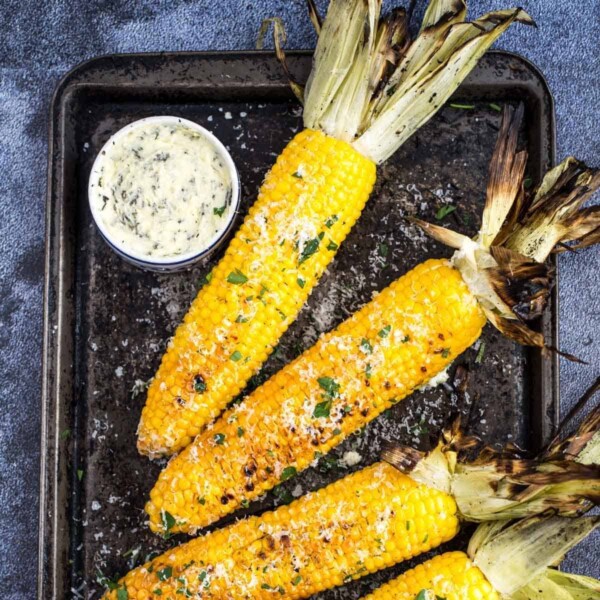 Grilled Corn on the cob on a platter with herb compound butter.
