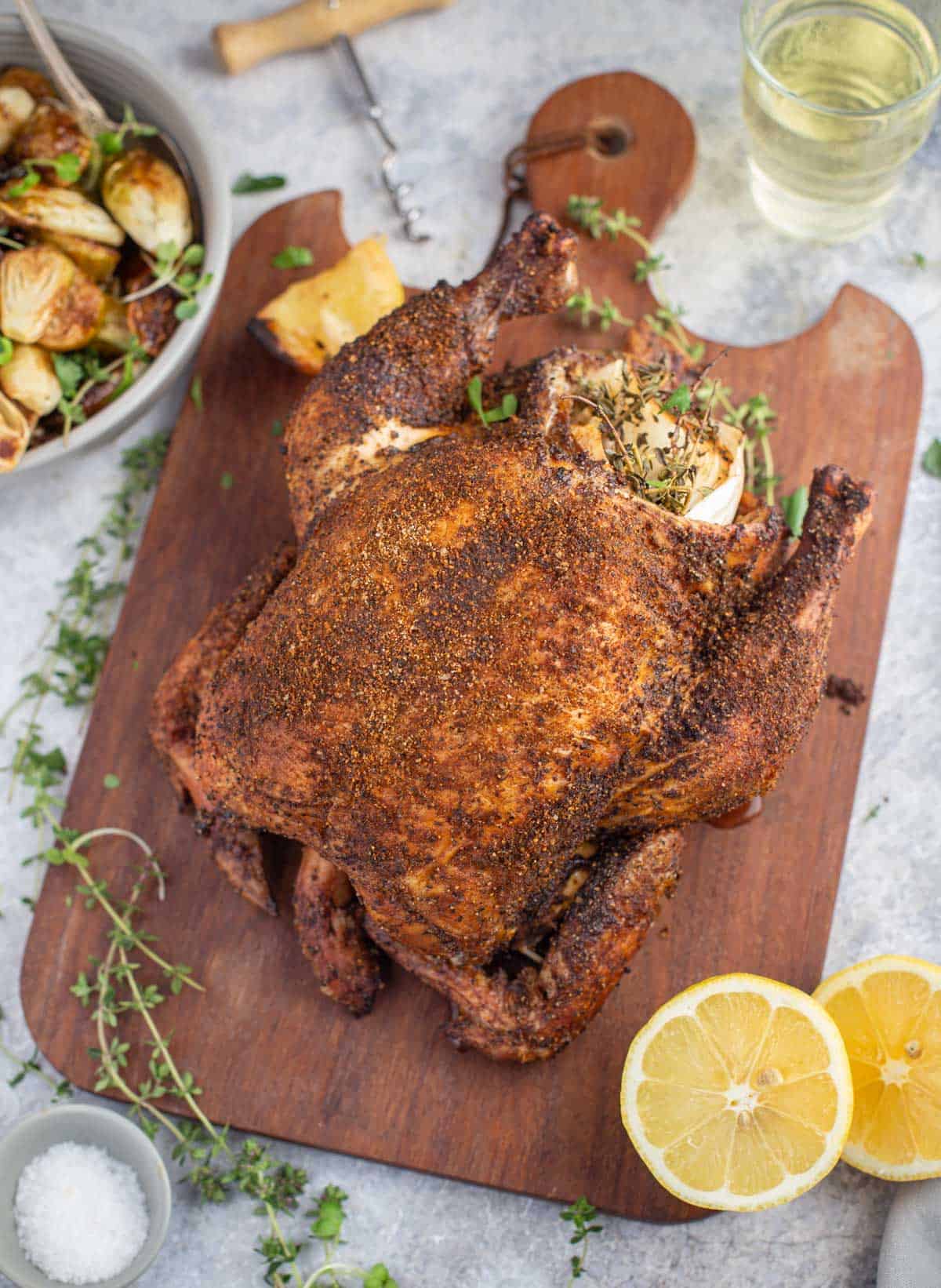 A whole chicken grilled in a pellet smoker on a cutting board 