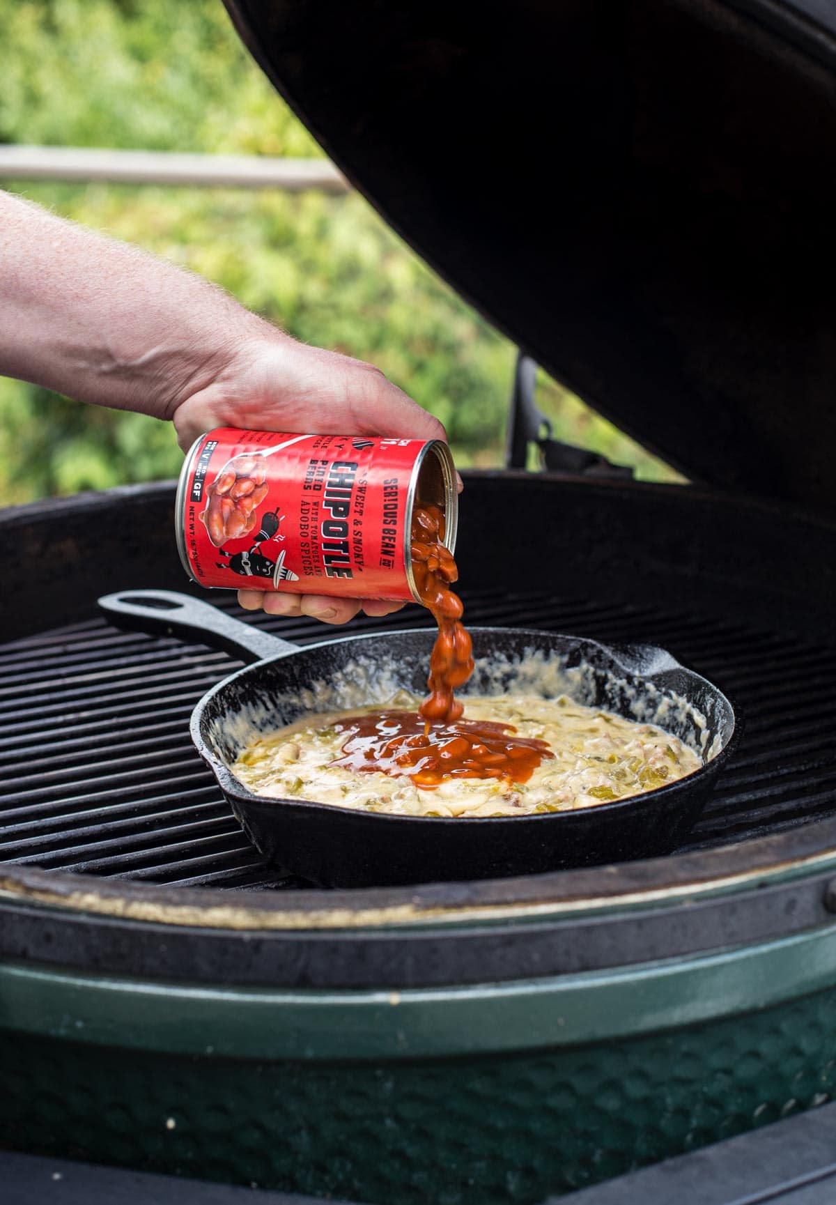 Pouring a can of beans into a queso dip on a grill