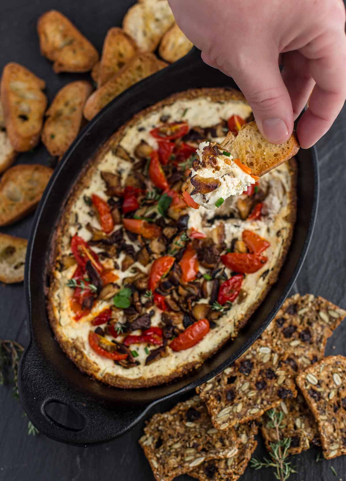 Cast iron dish with baked goat cheese dip, mushrooms, and crostini.