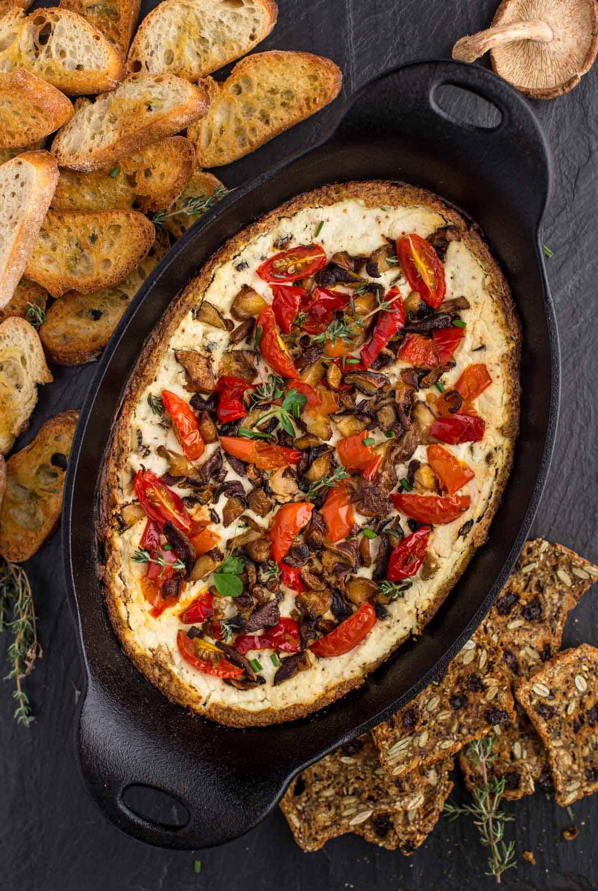 Goat Cheese Dip With Shitake Mushrooms, pickled peppers, and tomatoes in a serving platter with some baguette on the side