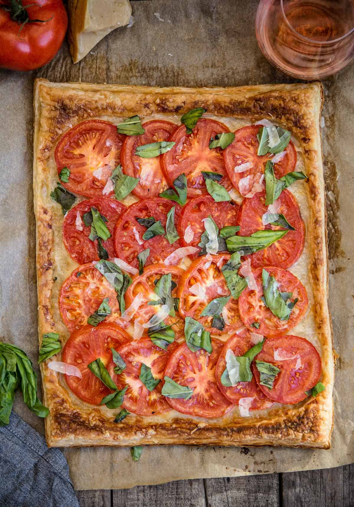 A fresh summer tomato galette on a serving platter with a glass of wine