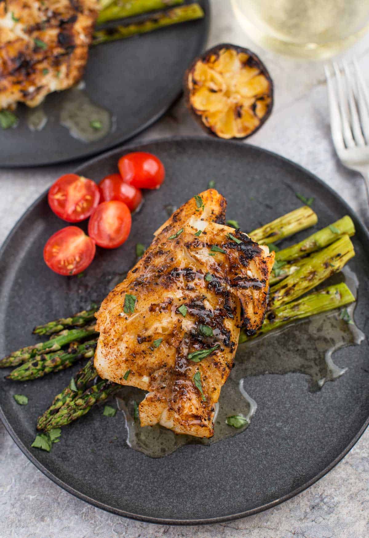 Grilled Cod with White Wine Butter Sauce on a plate with grilled asparagus and cherry tomatoes