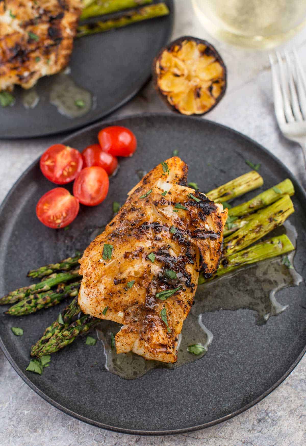 Grilled Cod with White Wine Butter Sauce on a plate with grilled asparagus and cherry tomatoes 