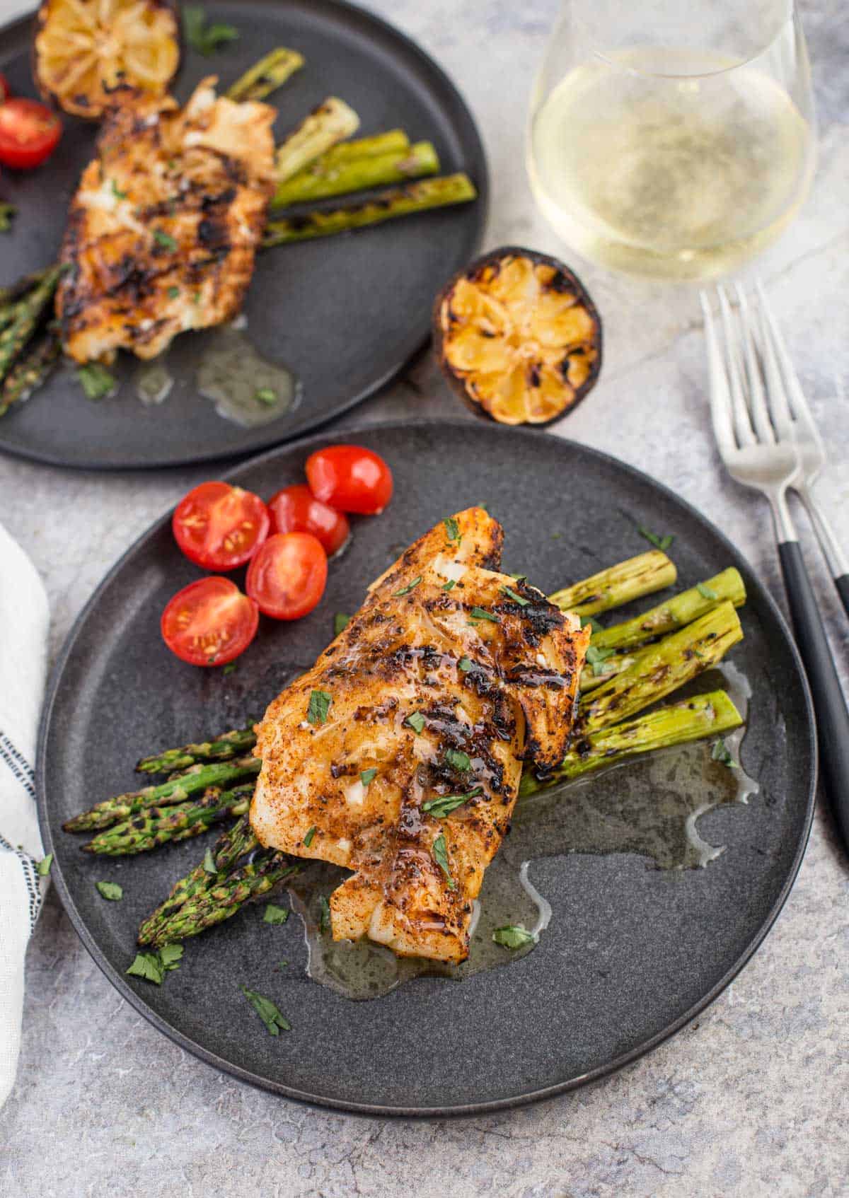 Grilled cod with white wine butter sauce on a platter with grilled asparagus