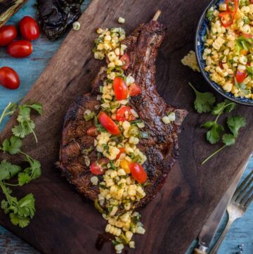 Roasted Poblano and Corn salsa over the top of a grilled ribeye steak on a cutting board.