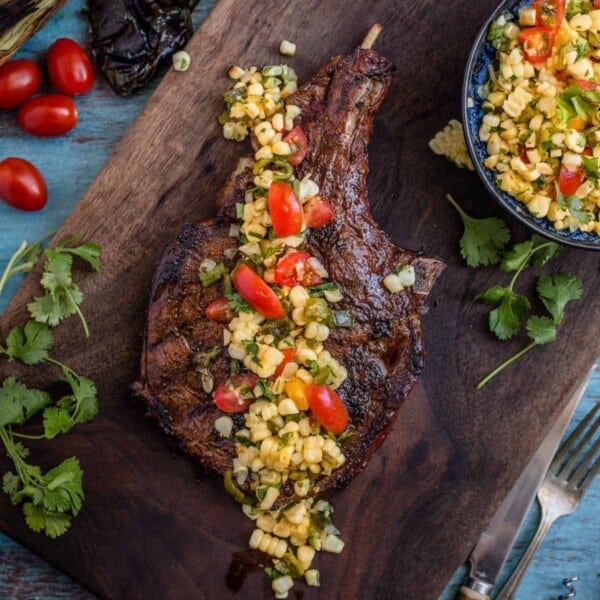 Roasted Poblano and Corn salsa over the top of a grilled ribeye steak on a cutting board.
