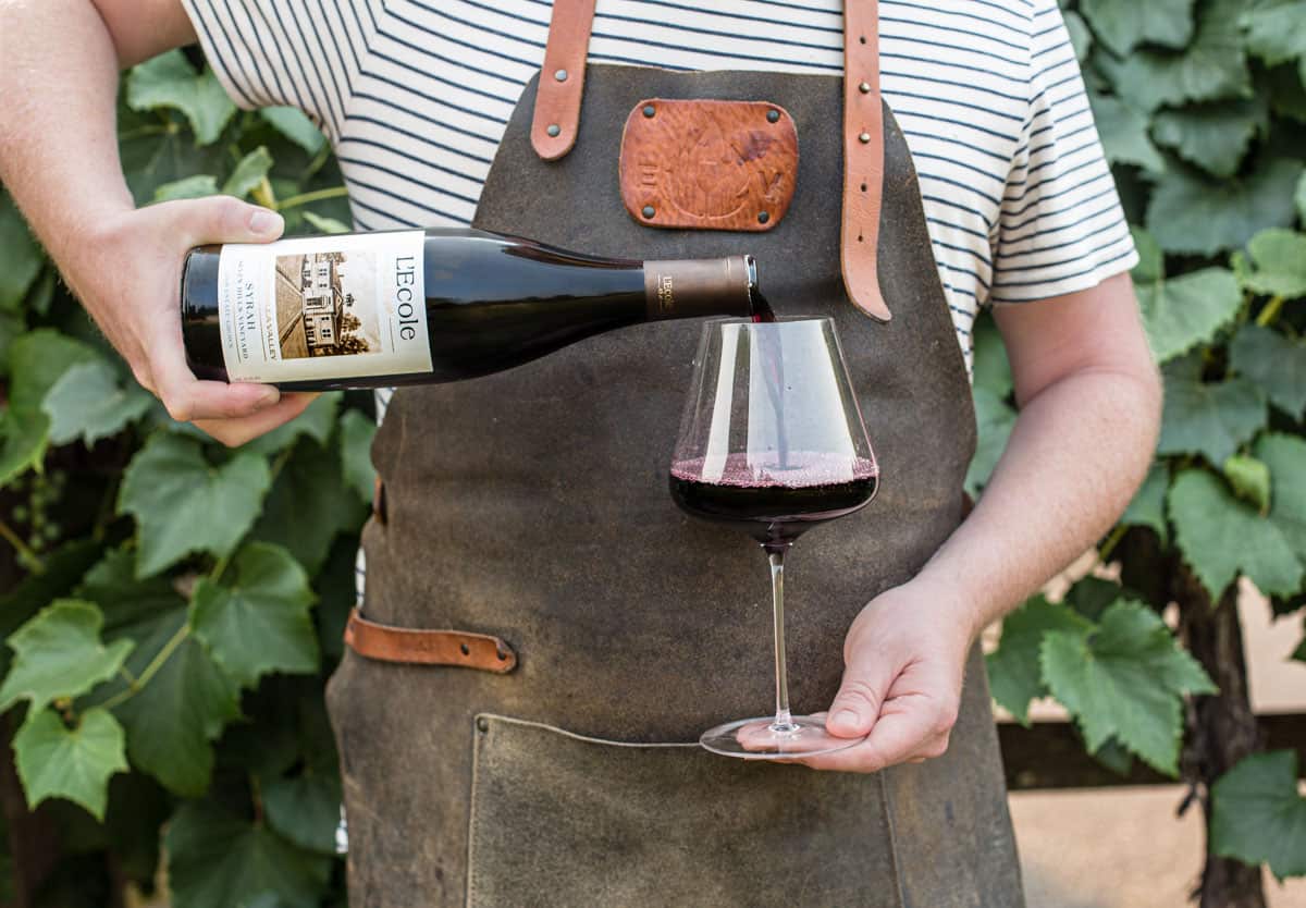 Pouring a glass of L'Ecole Syrah wine into a wine glass