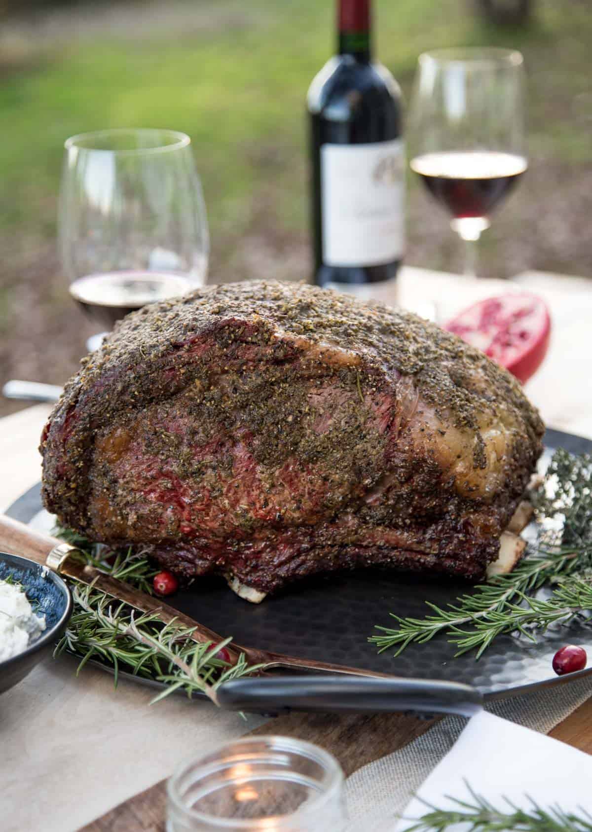 A smoked prime rib on a platter with a bottle of Syrah wine in the background