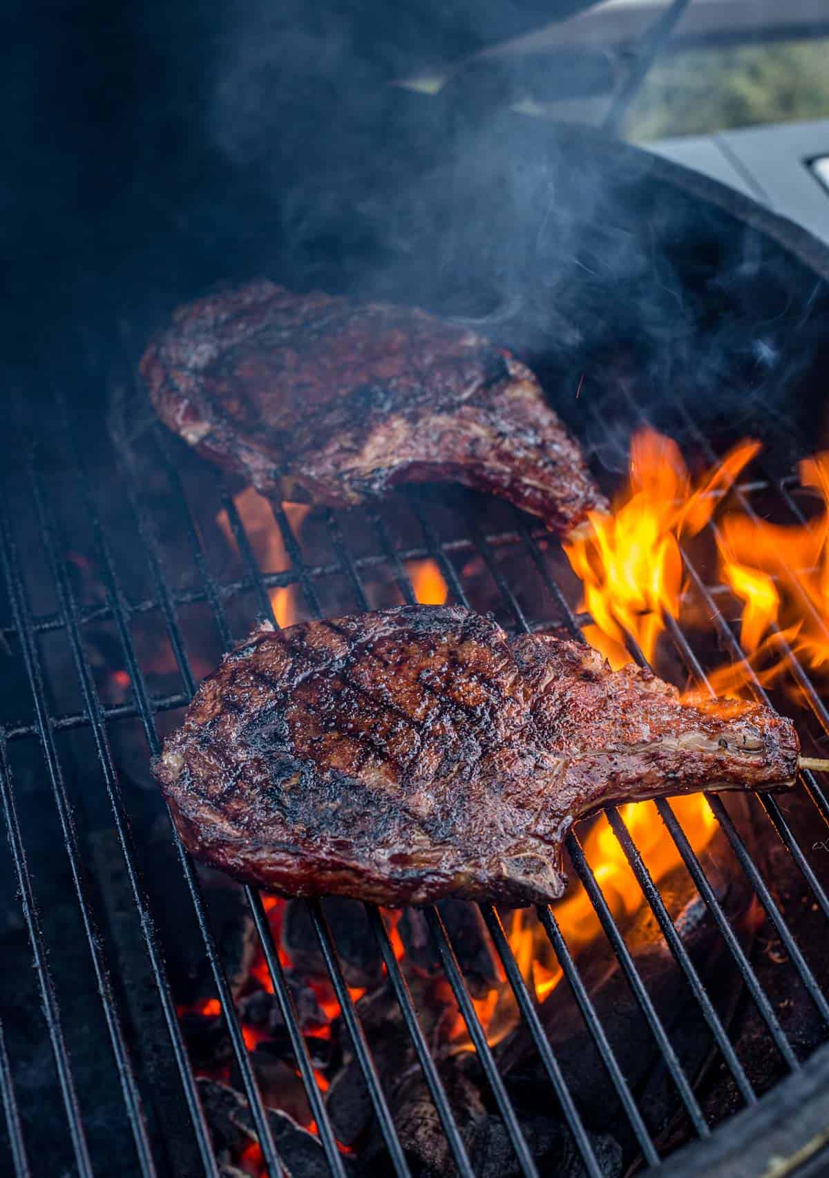 Two grilled ribeyes over a flame