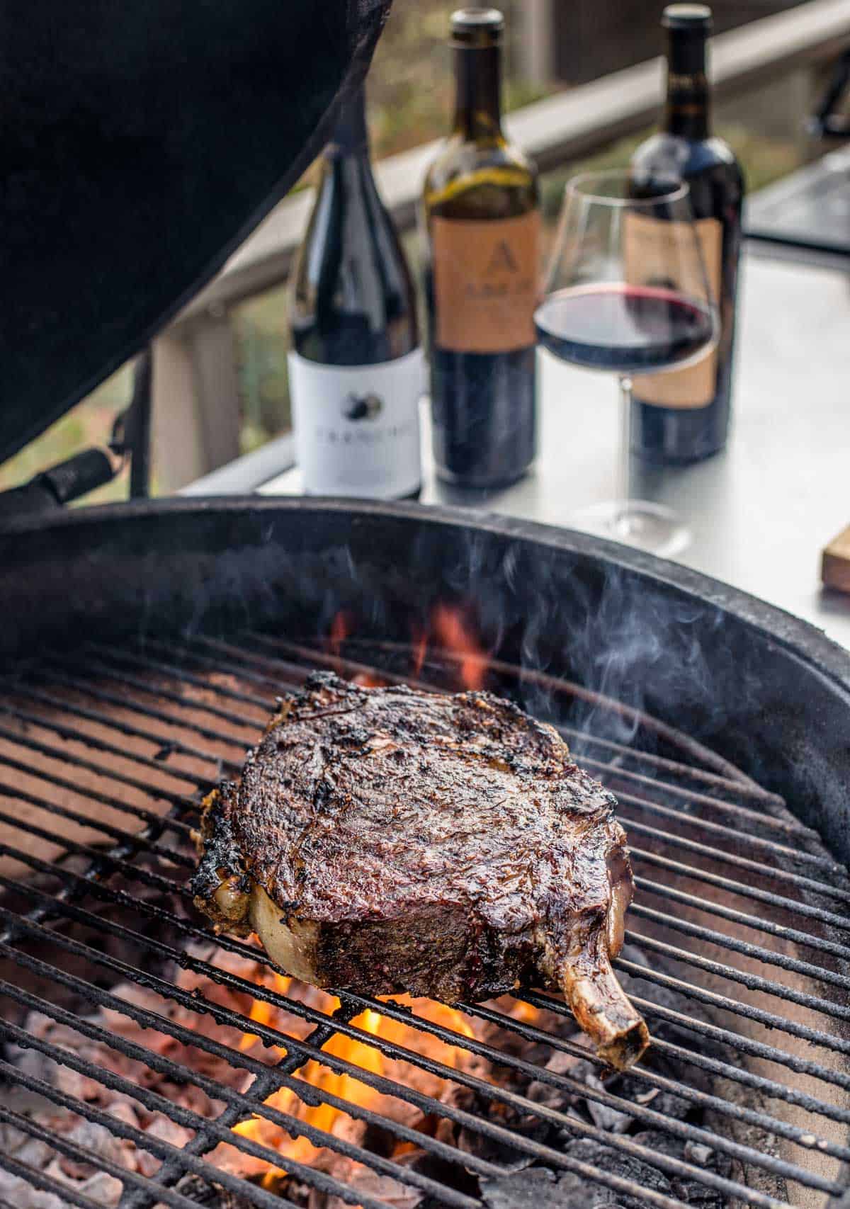Cowboye ribeye over direct heat with Cabernet Sauvignon wine in background.