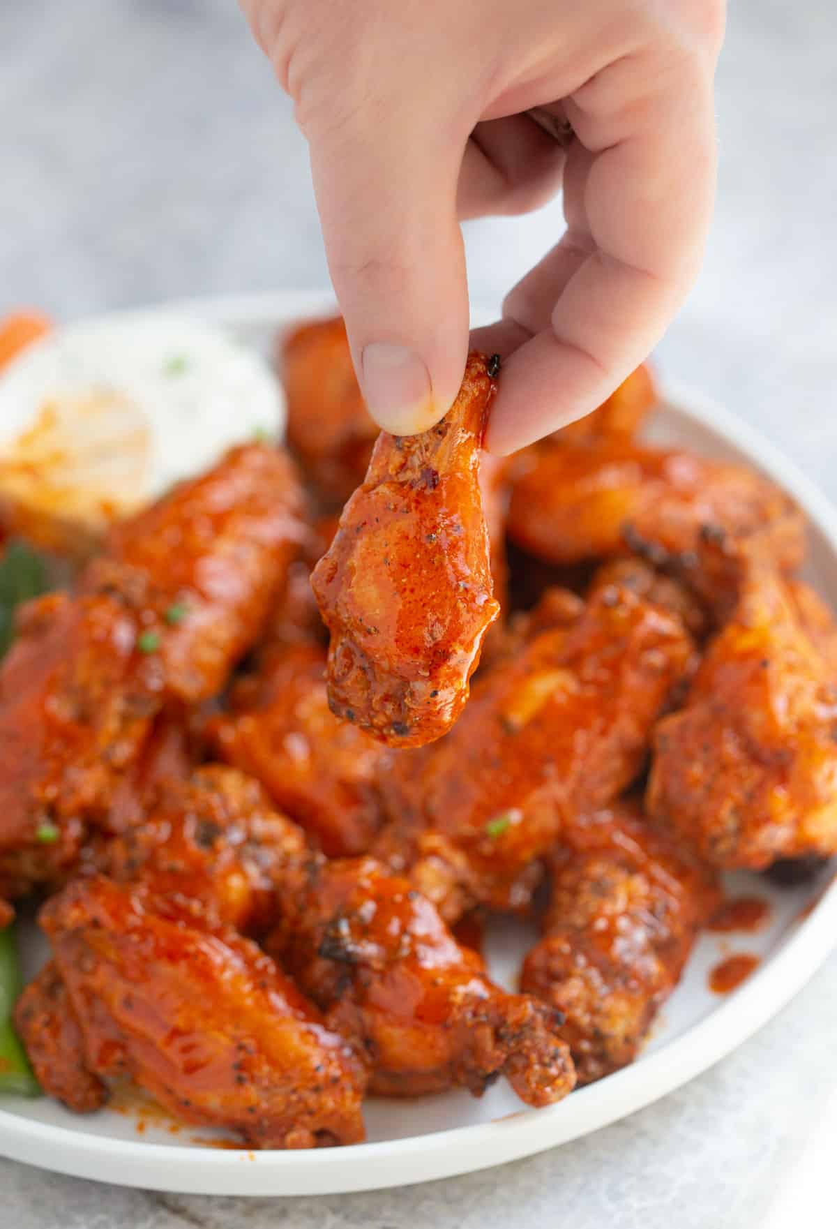 A hand grabbing a grilled Buffalo style chicken wing