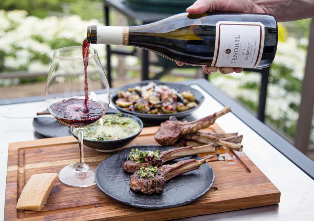 A glass of red wine being poured next to a plate of grilled lamb chops for a great wine and food pairing