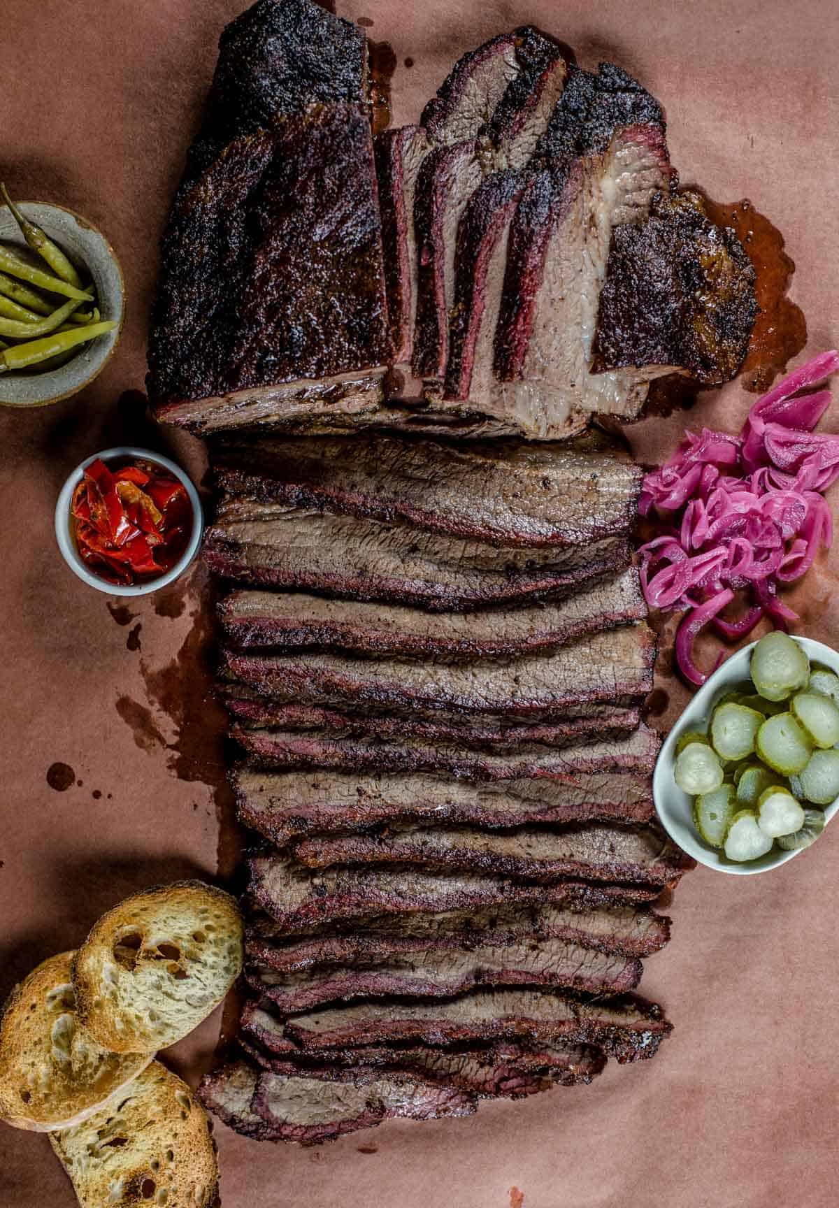 Smoked brisket sliced on pink butcher paper with garnishes