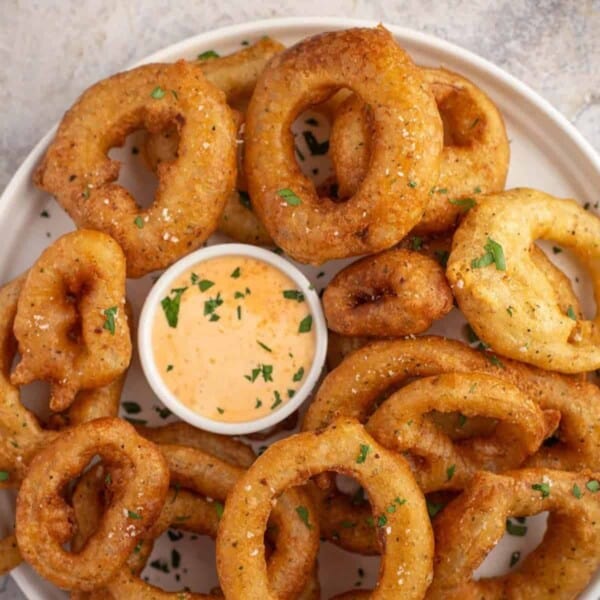 Beer Battered onion rings on a platter with dipping sauce.
