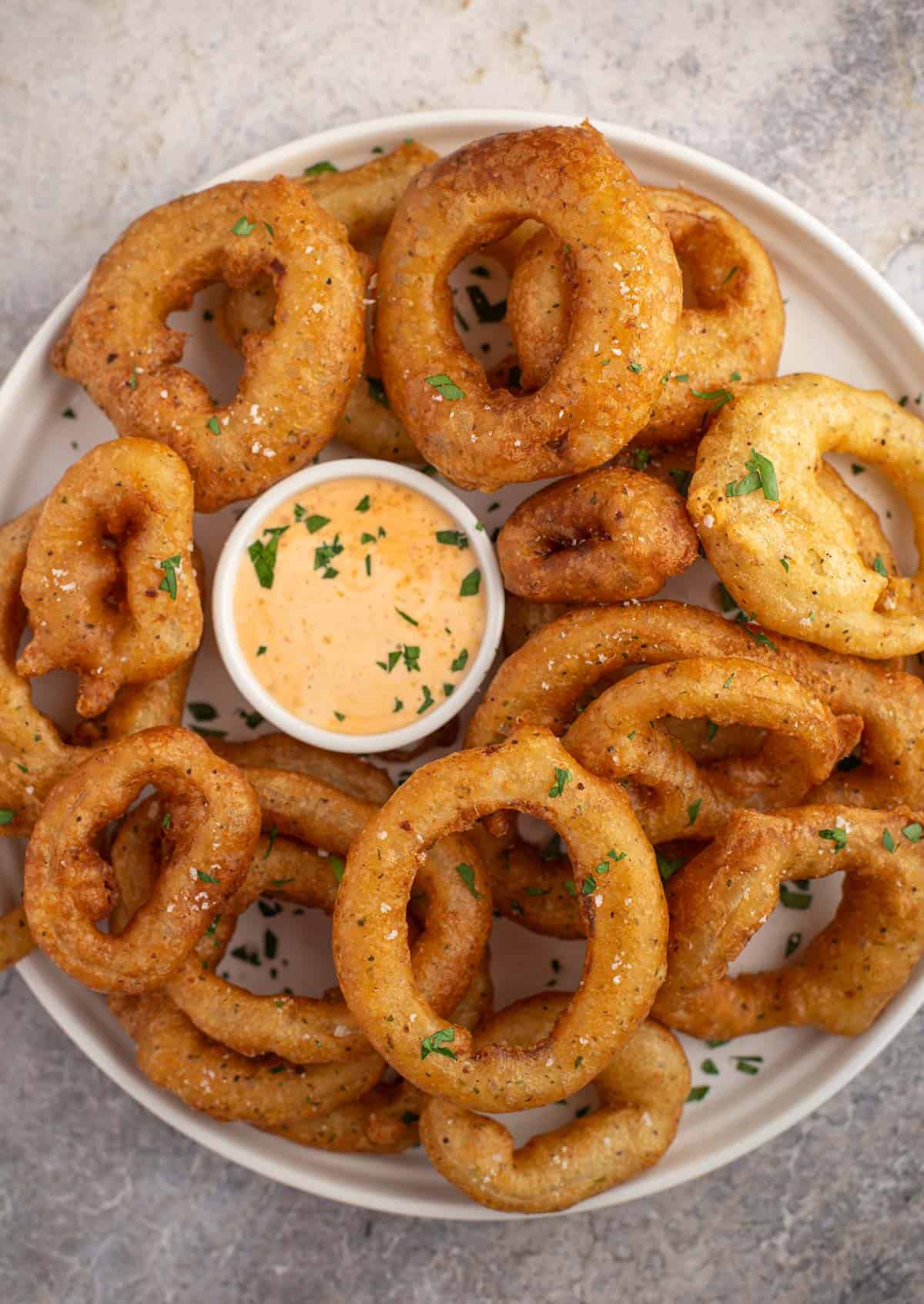 A platter full of smoked onion rings with a chipotle dipping sauce