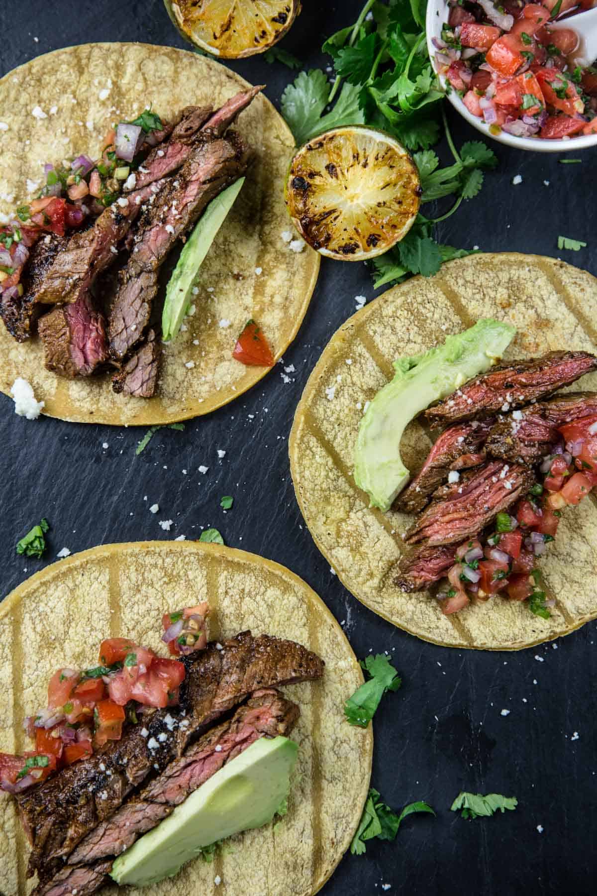 Three Carne Asada Steak Tacos made with Skirt Steak on a black platter