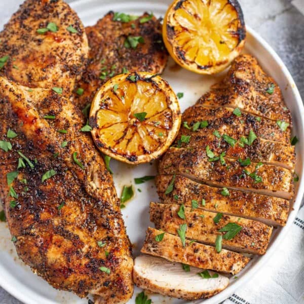 Two Grilled Boneless Skinless Chicken Breasts on a white plate with grilled lemon halves