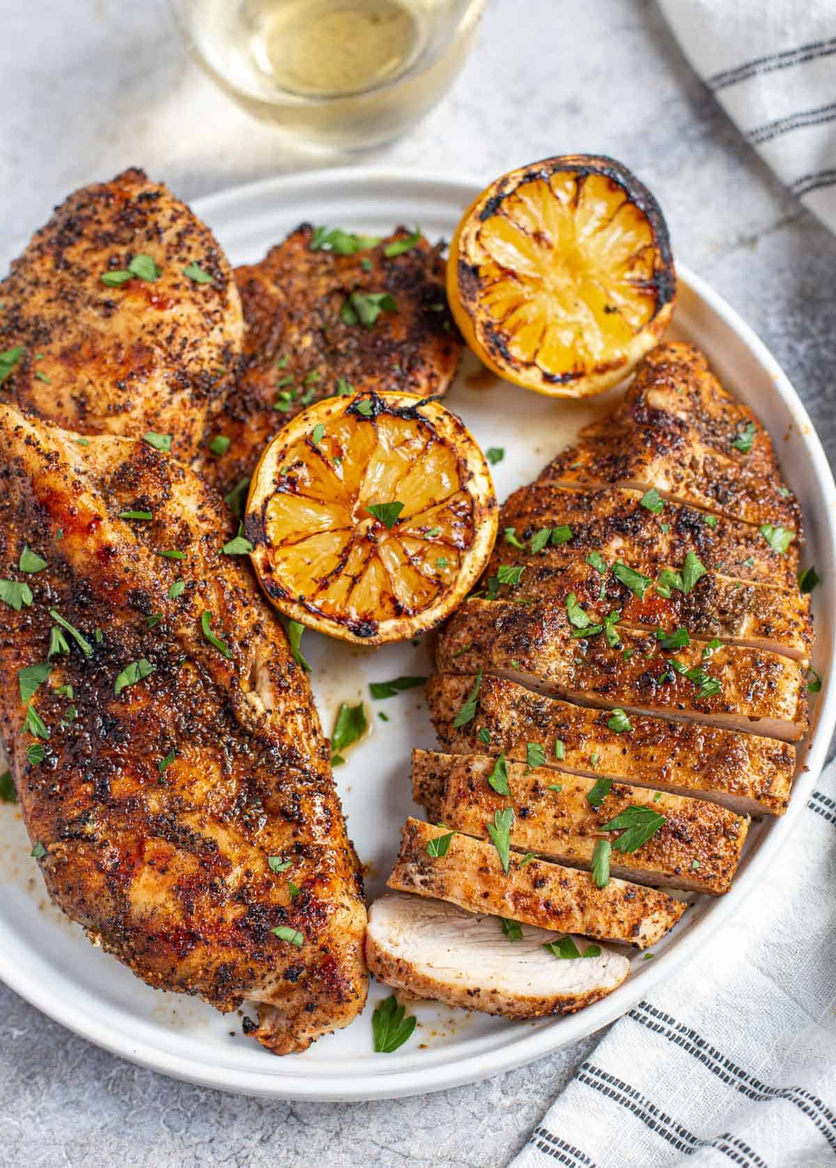 Grilled boneless skinless chicken on a plate with grilled lemon garnish.