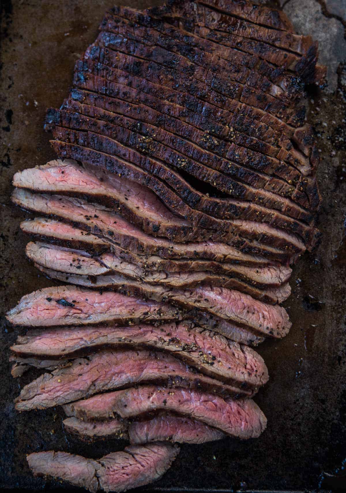 Slices of grilled flank steak on a sheetpan 