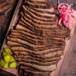 Smoked brisket flat on a cutting board with pickles and pickled onions.