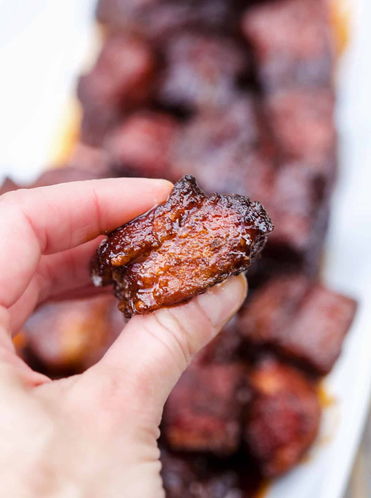 A hand holding a single smoked pork belly burnt end bite