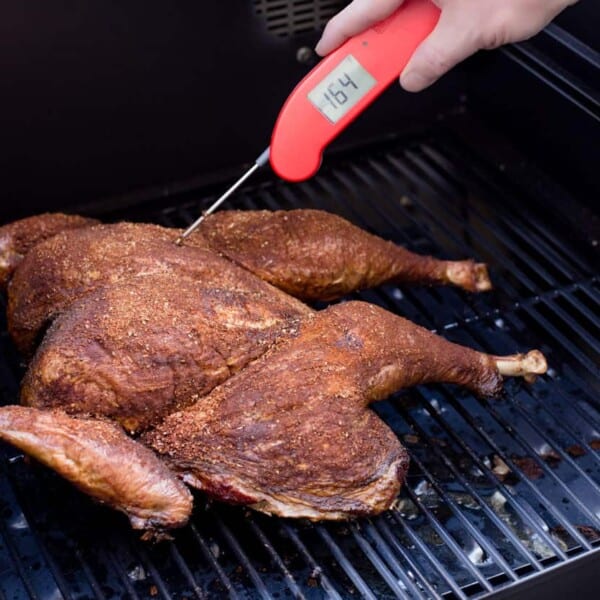 taking the temperature of a spatchcocked turkey on the grill