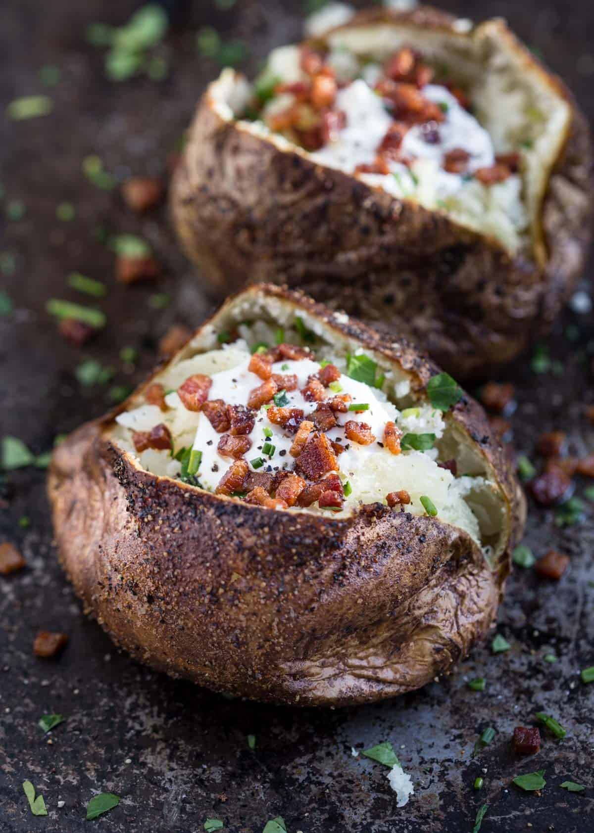 A grilled baked potato topped with sour cream, bacon, and chives 