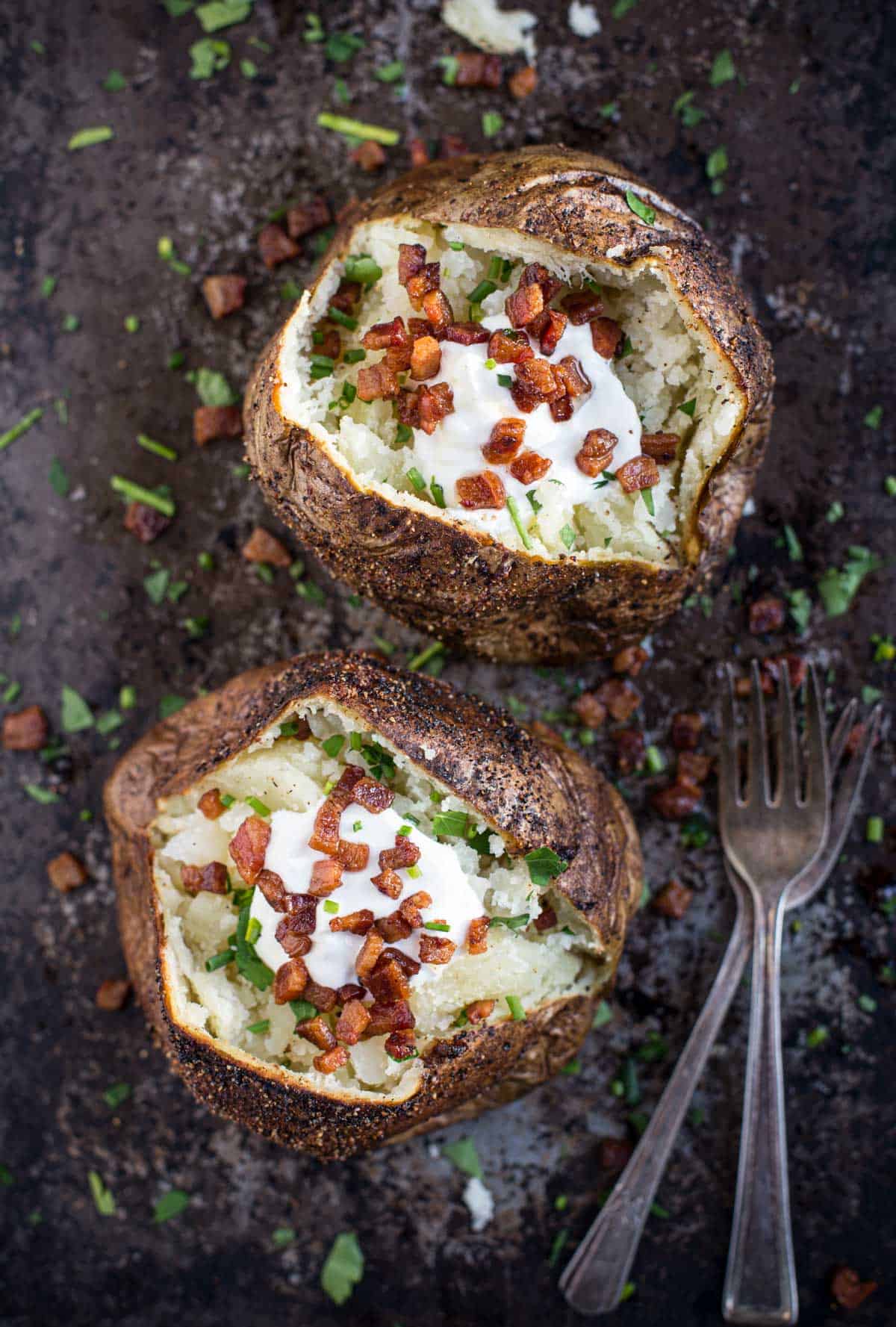 Two Grilled Baked Potatoes topped with sour cream and bacon on a sheetpan