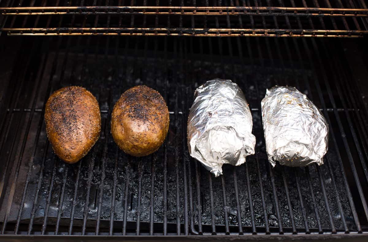 four potatoes on the grill. two wrapped in foil, the other two are not wrapped in foil