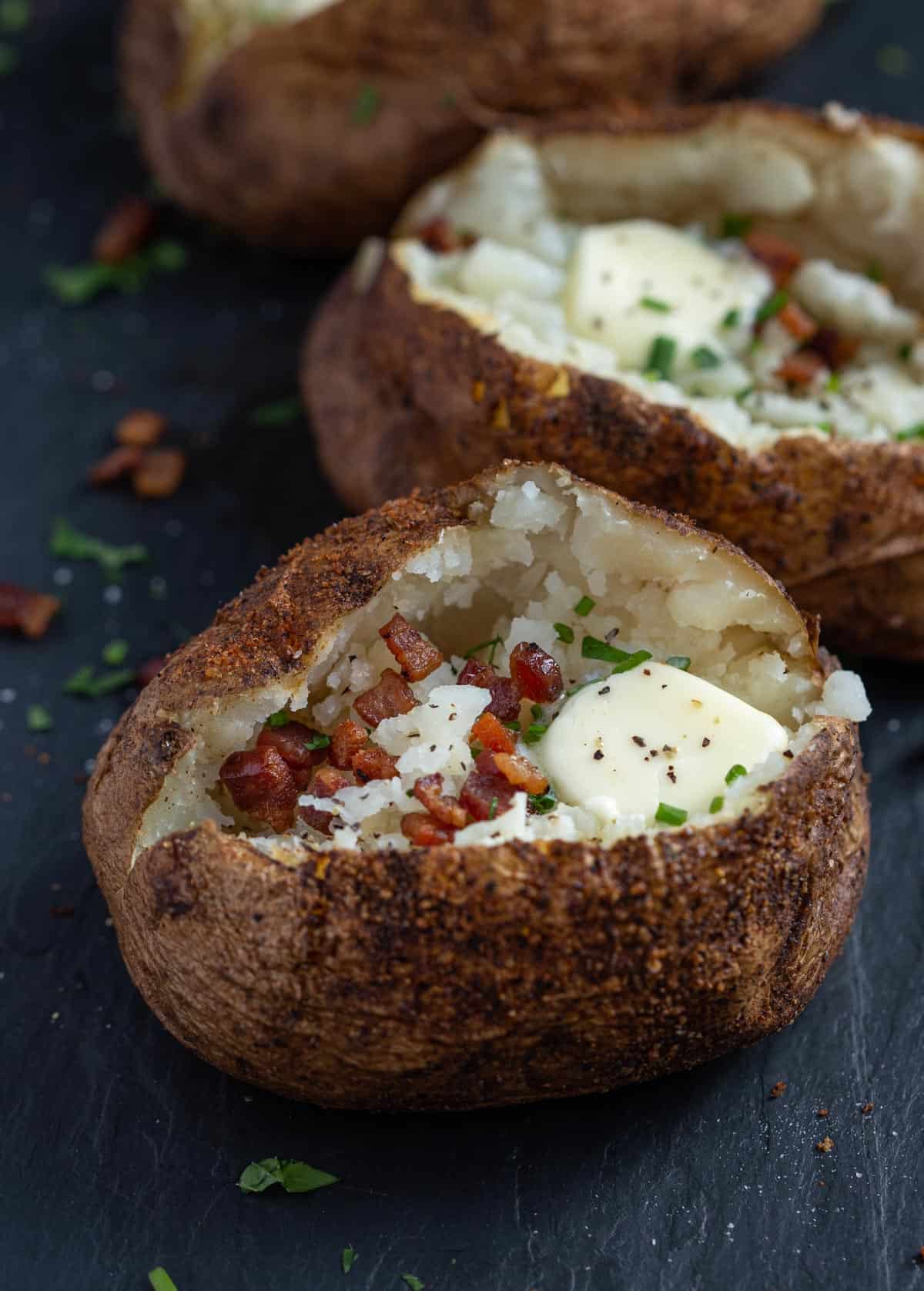A smoked baked potato topped with bacon, butter, and chives