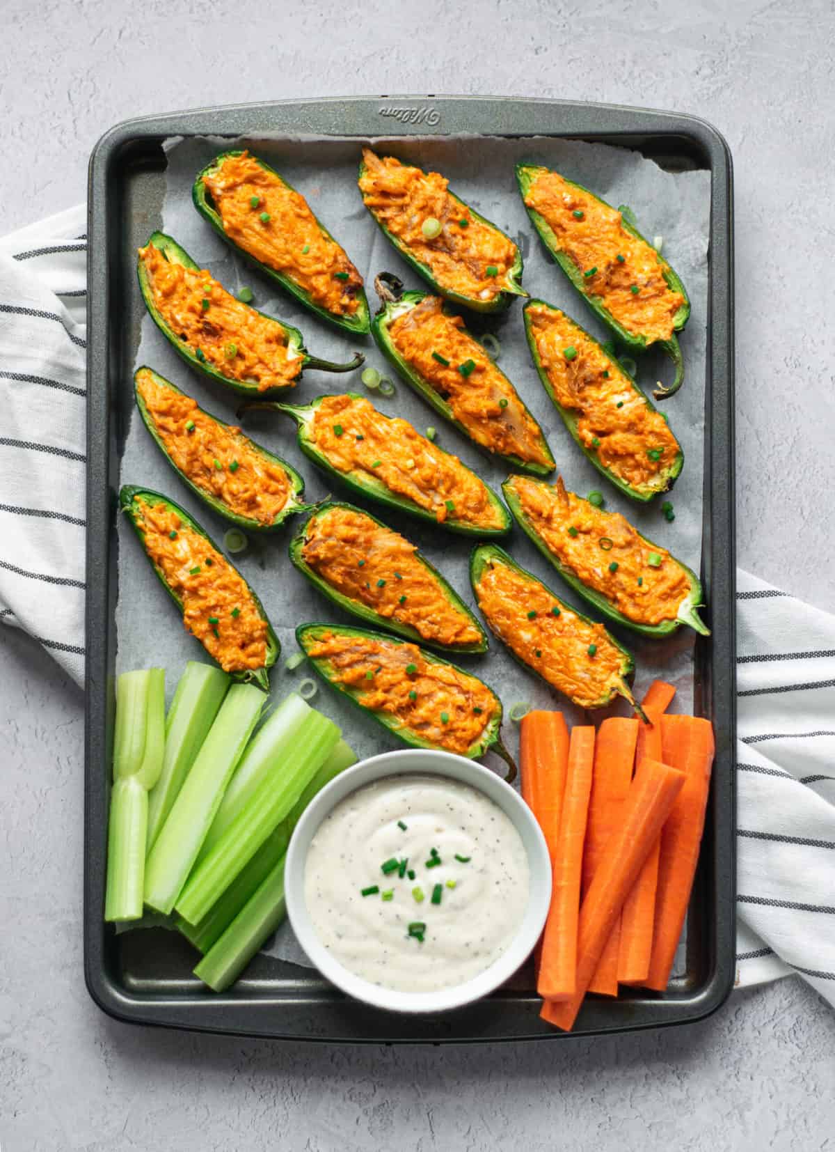 A tray of jalapeno poppers, celery sticks, carrots, and dipping sauce