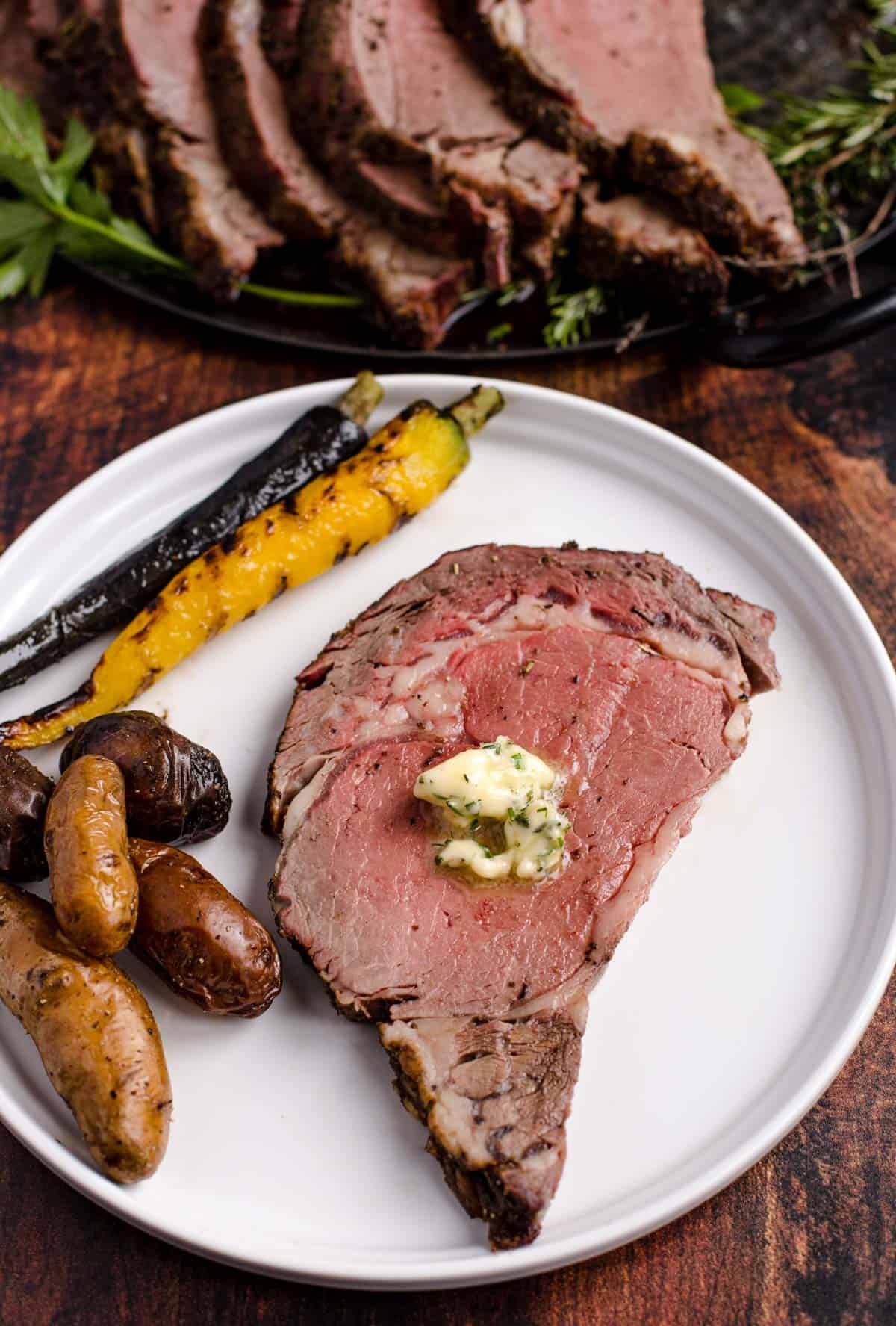 A slice of Grilled Prime Rib on a plate with herb compound butter and a side of vegetables