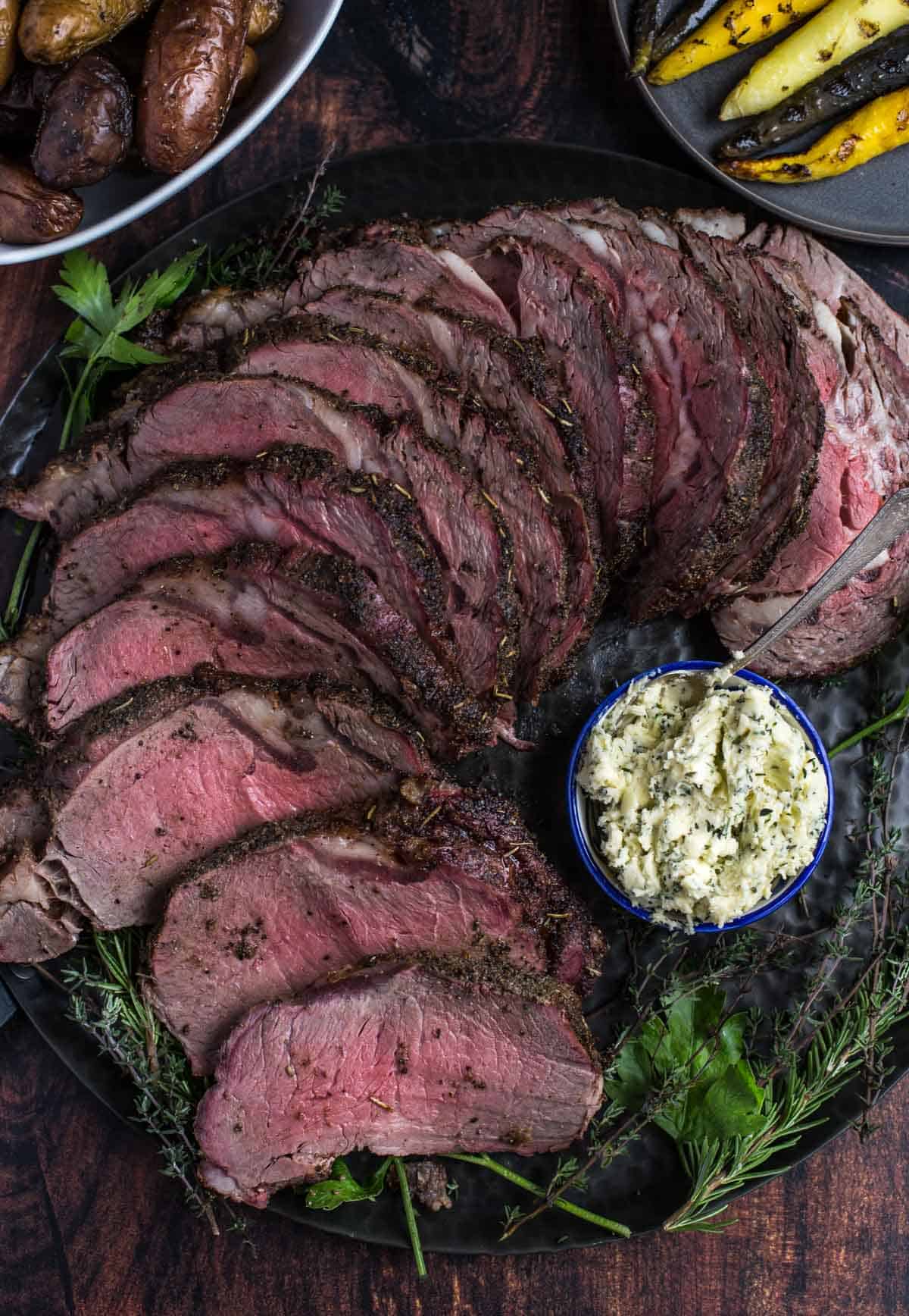 Slices of Grilled Prime Rib on a platter with a bowl of herb compound butter