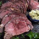 Slices of Grilled Prime Rib on a platter with a side of herb compound butter