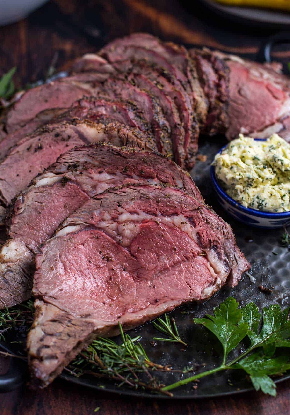 Slices of Grilled Prime Rib on a platter with a bowl of herb compound butter