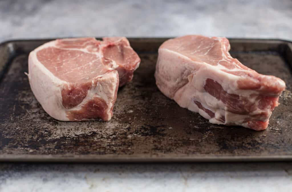 Side angle of two-inch thick bone in pork chops. One center cut chop and one rib chop.