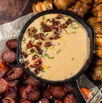 Beer Cheese Dip in cast iron pan on plate with pretzels and sausage.